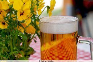 Ein Glas Bier und gelbe Blumen auf einer karierten Tischdecke