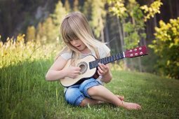 Musik für Kinder: Ein Mädchen sitzt auf einer Wiese und spielt Gitarre