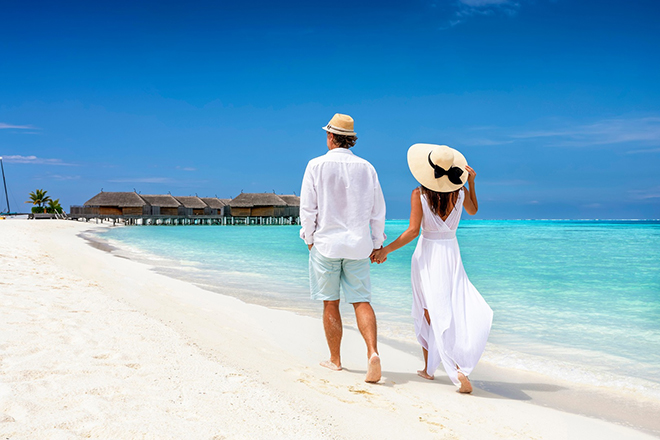 Happy couple in white clothing and with hats walks down a tropic